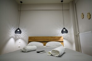 En snyggt bäddad säng med vita sängkläder, två svarta hänglampor och en sänggavel i trä.