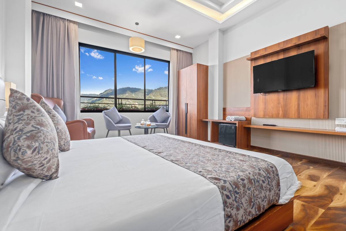 Een hotelkamer met een groot bed, een bureau, een televisie en uitzicht op de bergen.