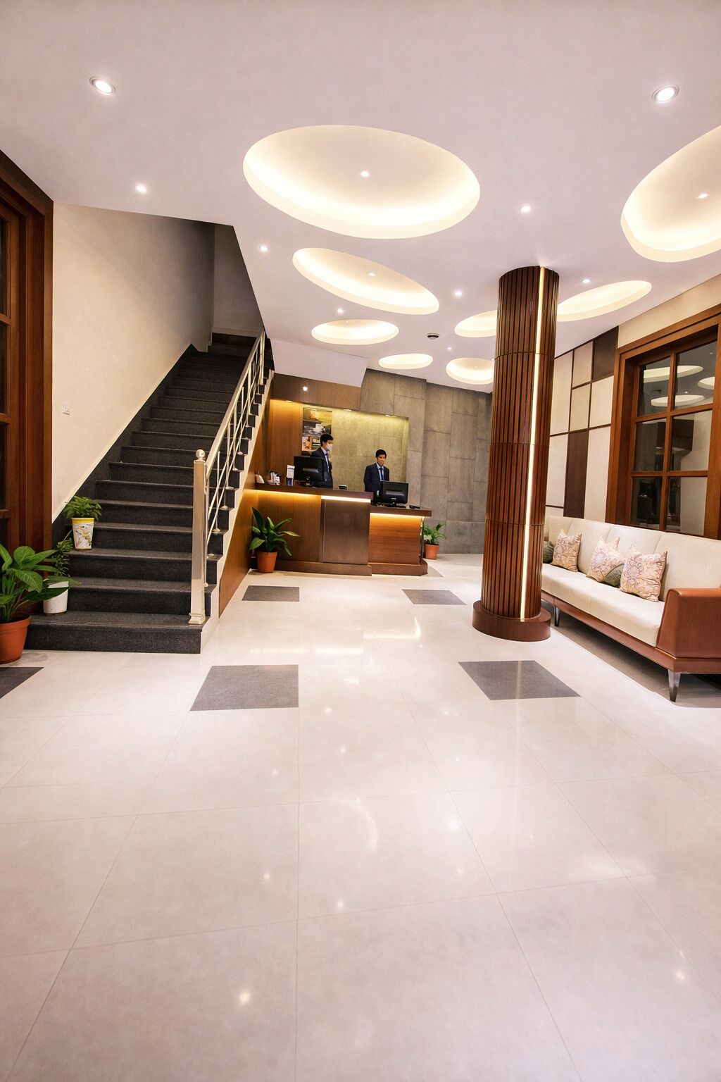 A hotel lobby with a reception desk, a staircase, a sofa, and a tall column.