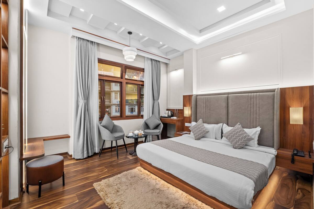 Een moderne hotelkamer met een groot bed, een bureau, twee stoelen, een kleine tafel en een raam met gordijnen.