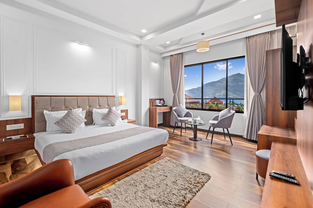 Een moderne hotelkamer met een groot bed, een televisie, een balkon met uitzicht en een kleine tafel met stoelen.