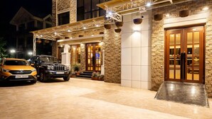 A hotel entrance with stone facade, a covered outdoor area, and a car parked in front.