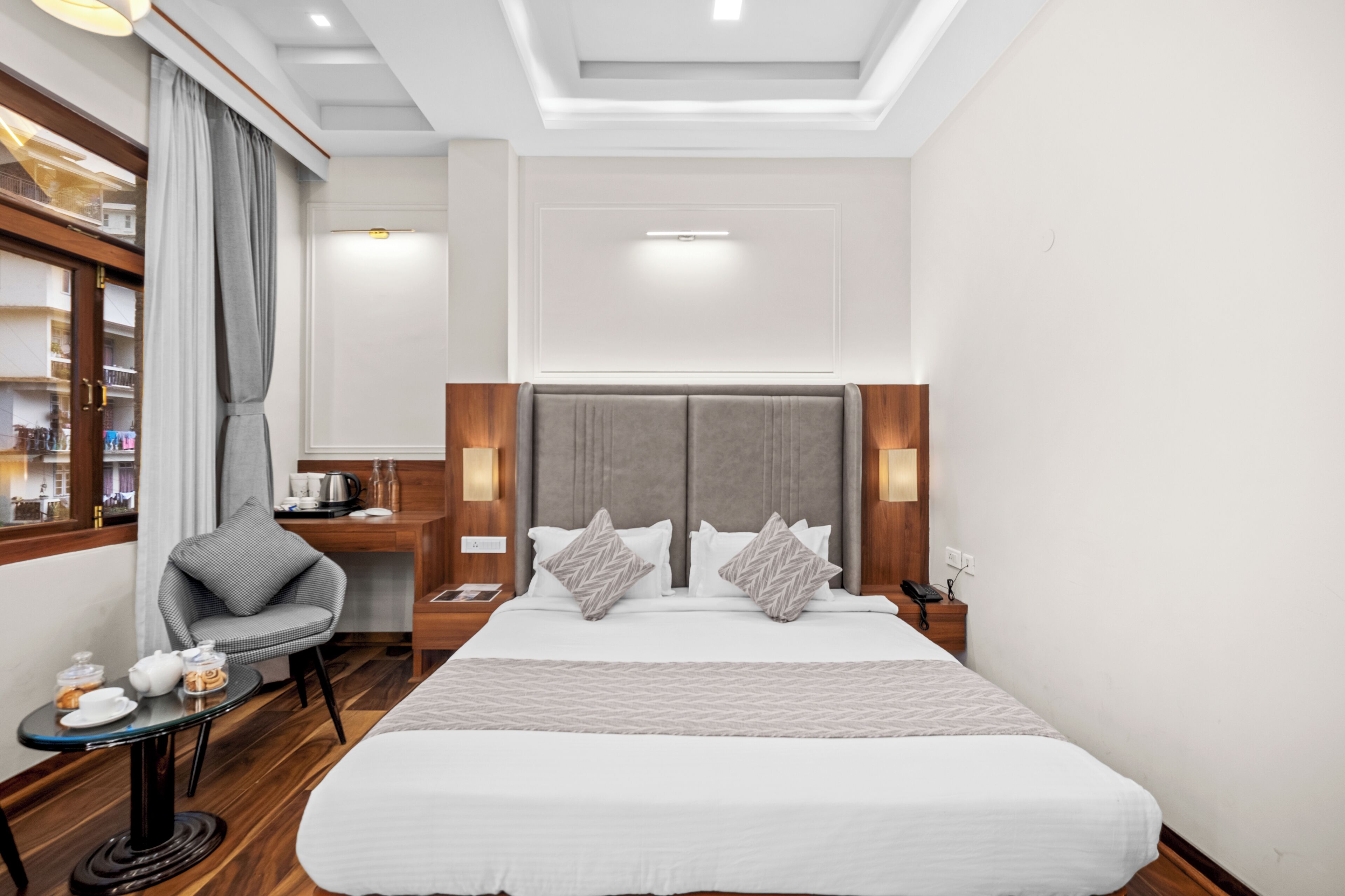 Une chambre d’hôtel avec un grand lit, un bureau avec une chaise, une petite table avec quelques objets et une fenêtre avec des rideaux.