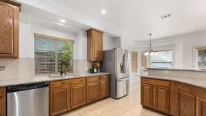 A modern kitchen with wooden cabinets, stainless steel appliances, and a large window with blinds. - Relaxed Family Home in Denton / Entire Home (Denton)