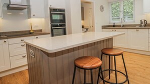 A modern kitchen with white cabinetry, a central island with stools, stainless steel appliances, and pendant lighting. - Ambwray (Ambleside)