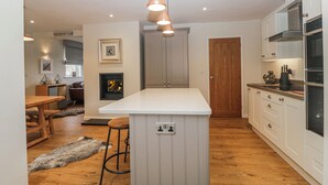 A modern kitchen with a central island, wooden flooring, and a fireplace. - Ambwray (Ambleside)