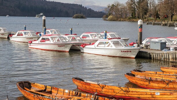 A marina with several small boats docked, a wooden dock, and a forested hill in the background. - Ambwray (Ambleside)