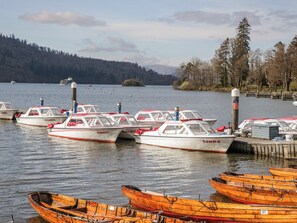 Ein Yachthafen mit mehreren kleinen Booten an einem Holzsteg, im Hintergrund ein bewaldeter Hügel.