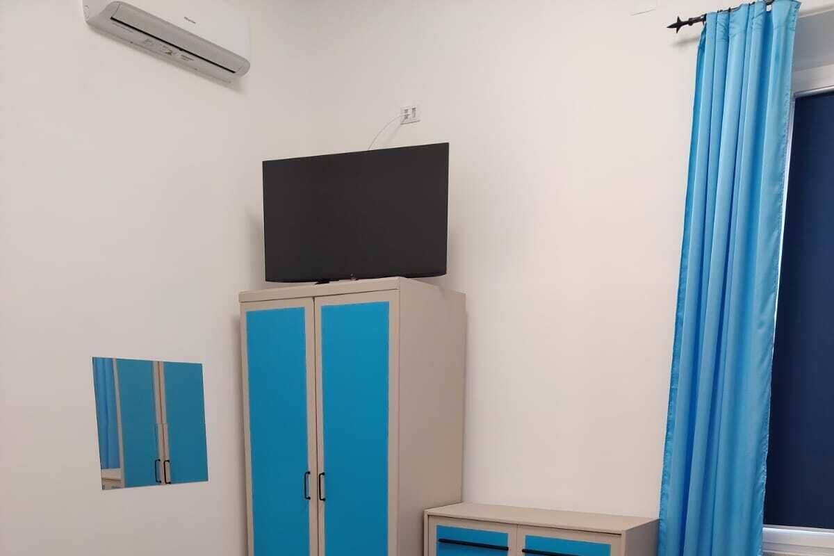 A bedroom with a bed, a wardrobe, a television, and a window with curtains.