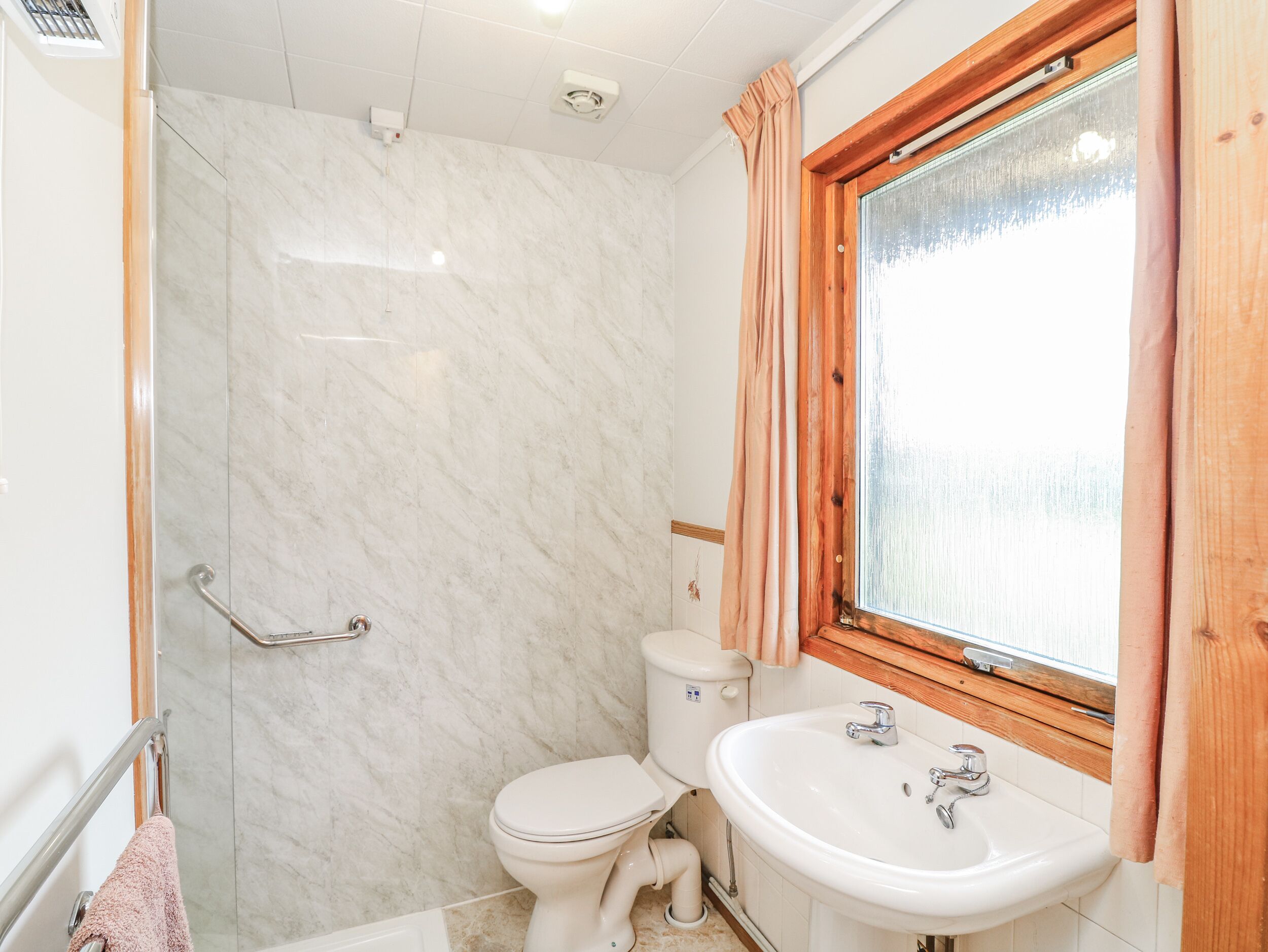 Ein Badezimmer mit Dusche, Toilette, Waschbecken und einem Fenster mit Vorhängen.