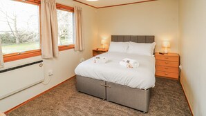 Un dormitorio con cama, dos mesitas de noche con lámparas, una ventana con cortinas y un radiador.