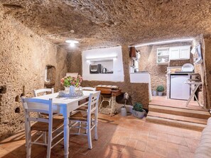Un intérieur rustique en pierre, comprenant un coin repas, une cuisine et un escalier menant à un niveau supérieur.