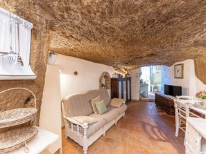 A rustic interior with a stone ceiling, a white sofa, a dining table, and a television. - Il Nido sulla Terrazza  (Pitigliano)