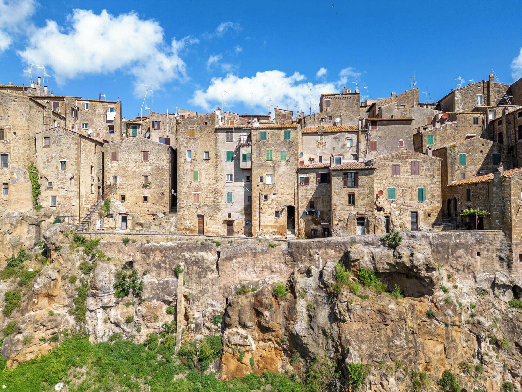 Un bâtiment en pierre à plusieurs étages, doté de fenêtres étroites et adossé à une falaise escarpée.