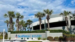 A resort entrance with a sign reading 'SeaWatch Resort,' palm trees, and a modern building structure. - Our beautiful, one bedroom beachfront condo (sleeps 6) has spectacular views of the Atlantic Ocean from the 17th floor! Newly updated in December 2025 (Myrtle Beach)