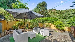 Une terrasse extérieure avec des meubles en osier, un grand parasol et une pelouse artificielle verte.