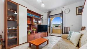 Un salon comprenant un canapé, un téléviseur, un meuble en bois et une porte-fenêtre coulissante donnant sur un espace extérieur.