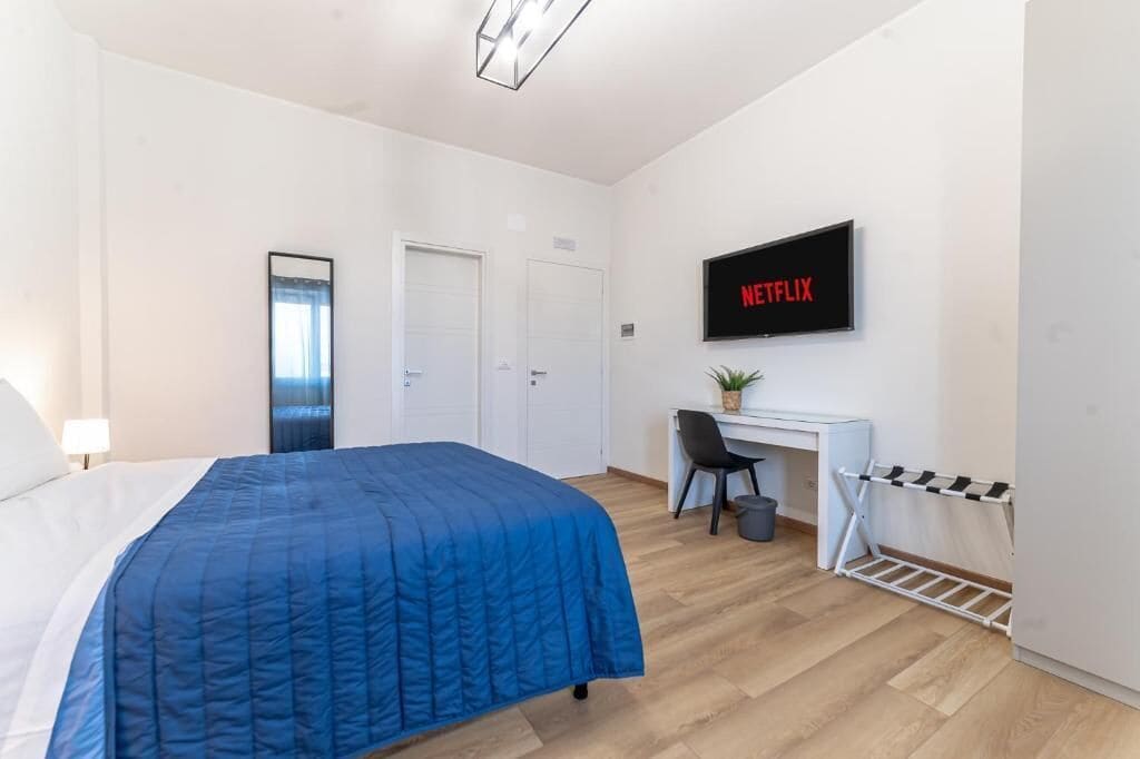Una habitación de hotel con cama, escritorio, silla, televisor mostrando 'NETFLIX' y un zapatero.