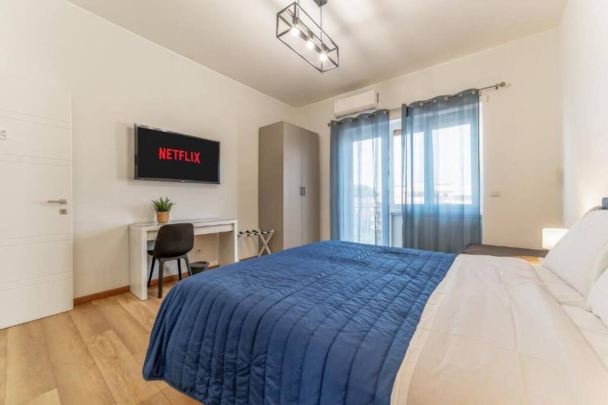 Ein Schlafzimmer mit einem Bett, einem Schreibtisch mit Stuhl, einem Fernseher und einem Fenster mit Vorhängen.