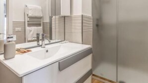 A modern bathroom with a white sink, mirror, and cabinets.