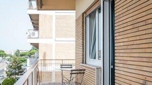 A balcony with a table and chairs, a view of the street, and a building with wooden paneling.