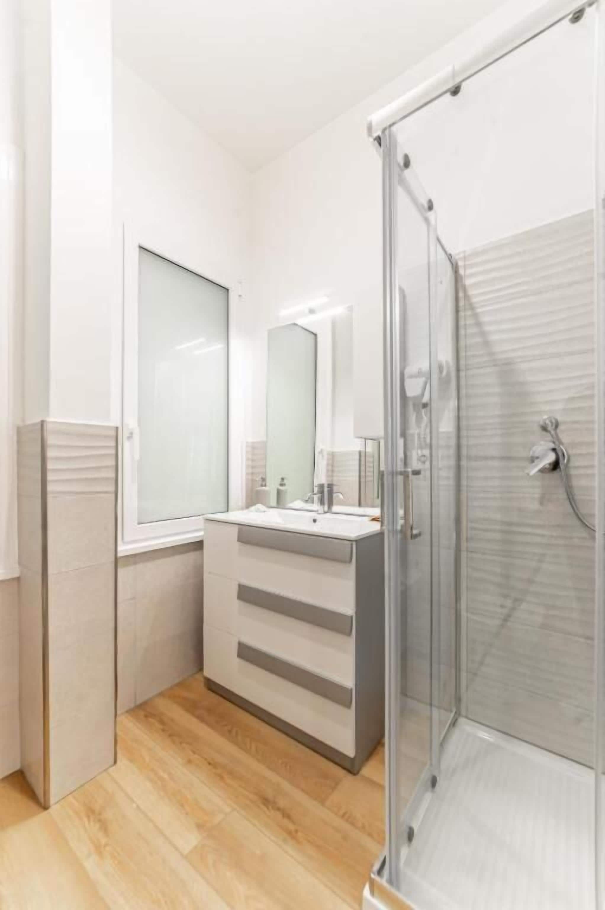 A modern bathroom with a glass shower enclosure, a large mirror, and a vanity with a sink.