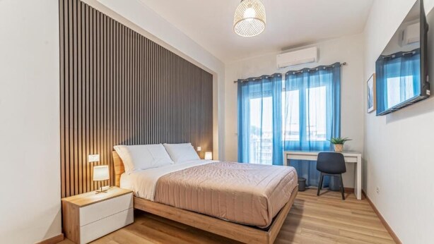 A bedroom with a bed, bedside table, lamp, and a desk with a chair.