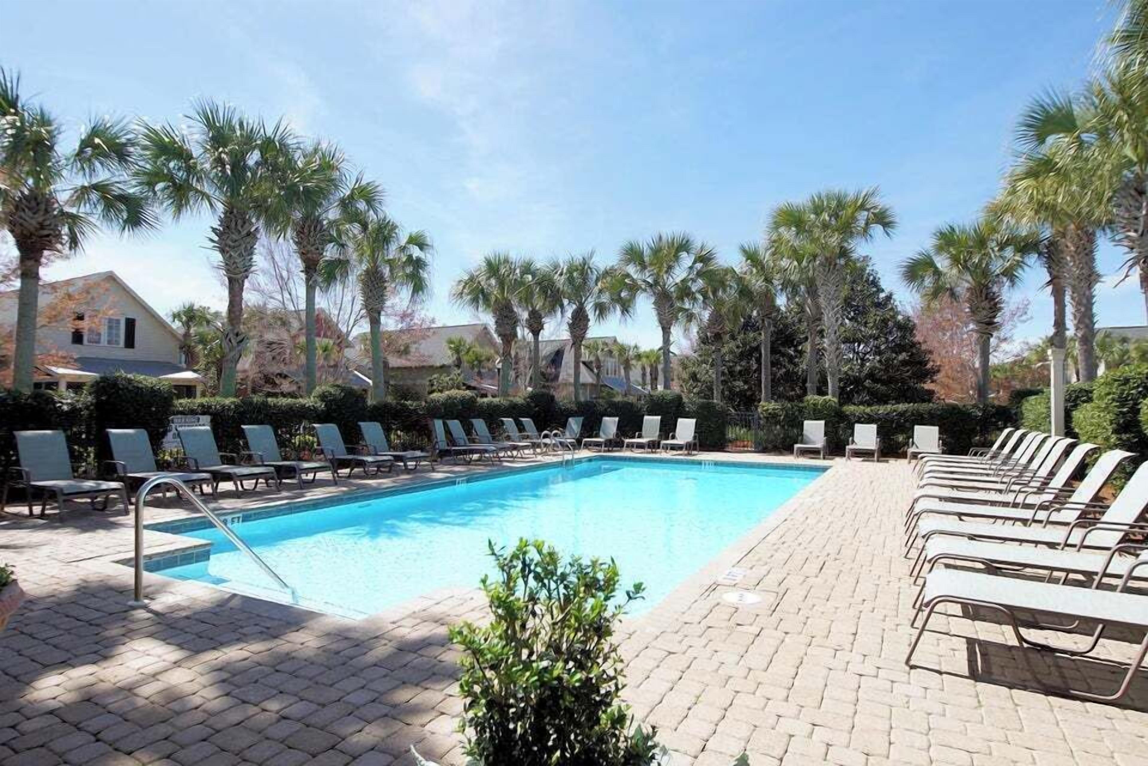 A swimming pool with lounge chairs, palm trees, and a brick pathway.