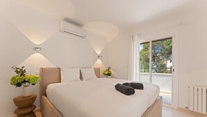 Ein modernes Schlafzimmer mit einem großen Bett, Nachttischen mit Pflanzen und Blick ins Freie durch eine Schiebetür.