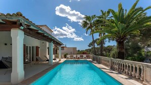 Ein Swimmingpool mit Liegestühlen, einer Pergola und Palmen.