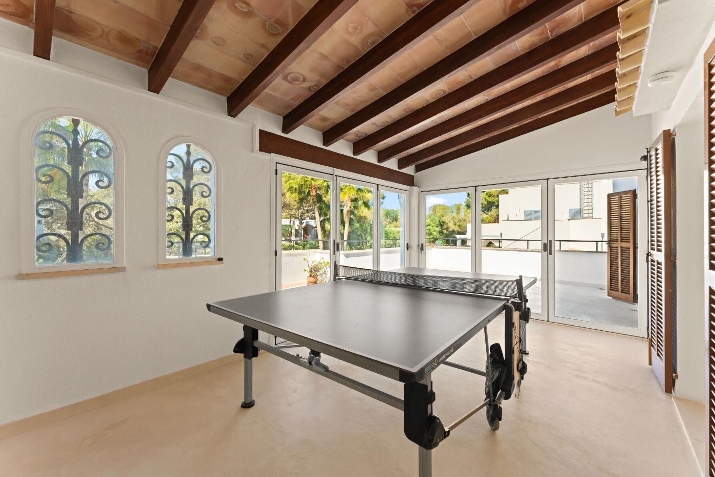 Una mesa de ping pong en una habitación con techo alto, ventanas amplias y vistas al exterior.