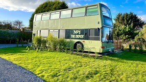 A double-decker bus parked in a grassy area with trees and a clear sky. - No 1 The Depot (Gateshead)