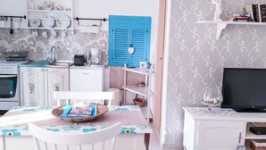 Une cuisine compacte dotée d’une porte à volets bleus, de meubles blancs et d’un coin repas avec une table et des chaises.