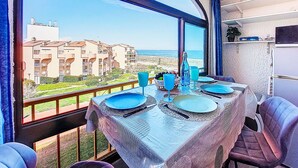 A dining area with a table set for four, a view of the beach, and a balcony with a railing. - Palm Beach by Interhome (Le Barcarès)