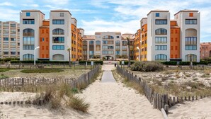 A beachfront hotel with a central pathway leading to the entrance, surrounded by sandy areas and wooden fences. - Palm Beach by Interhome (Le Barcarès)