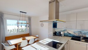 Una cocina moderna con estufa integrada, una ventana con vistas a árboles y un comedor con mesa y sillas de madera.