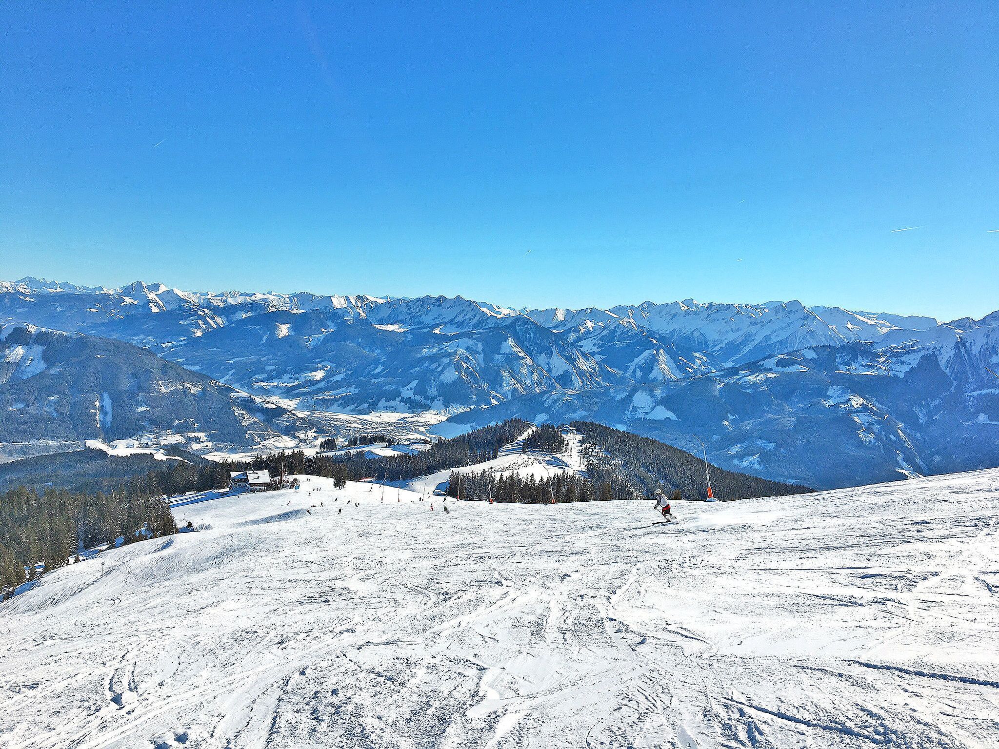 Un paysage de montagne enneigé, avec des pistes de ski et un ciel bleu dégagé.