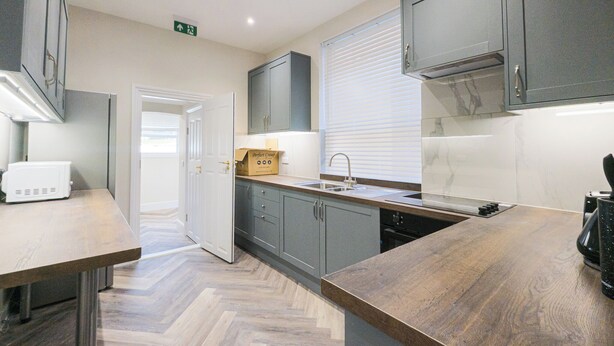 A modern kitchen with a herringbone wood floor, grey cabinets, a built-in oven, and a white countertop.