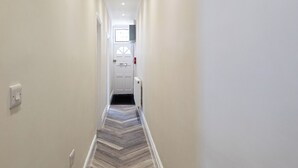 A narrow hallway with a herringbone-patterned floor, white walls, and a door at the end.