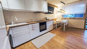 Et moderne køkken med hvide skabe, indbygget ovn, spiseområde med bord og stole samt et vindue med udsigt.