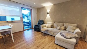 En moderne stue med sofa, lænestol, lille bord og en skydedør til en balkon.