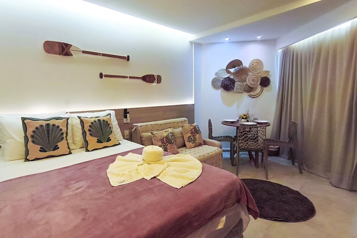 A hotel room with a bed, pillows, a bedside table, a chair, and a wall with decorative items.