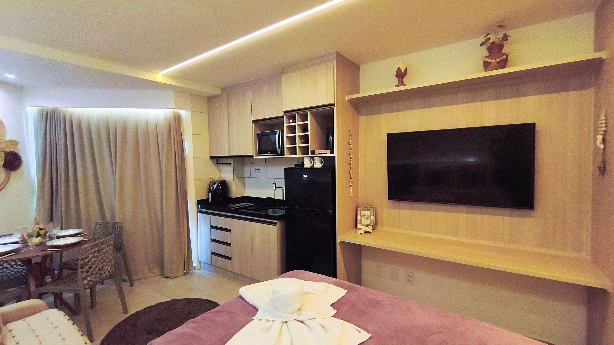 A compact living space with a kitchenette, a dining area, and a flat-screen TV mounted on the wall.