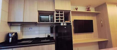 A compact kitchen with a microwave, a black refrigerator, and a flat-screen TV mounted on the wall.