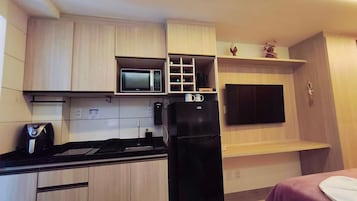 Cocina compacta con microondas, un refrigerador negro y un televisor de pantalla plana montado en la pared.