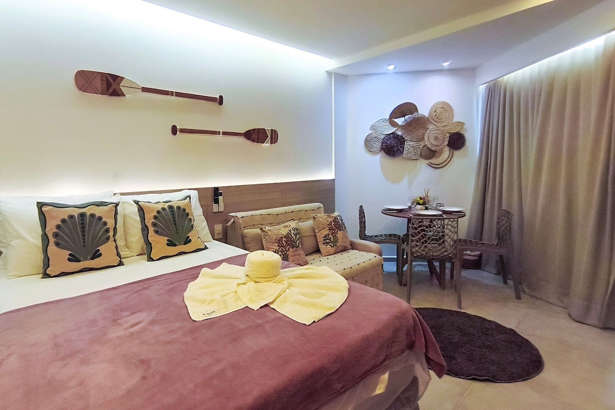 Quarto de hotel com cama, almofadas, mesa de cabeceira, cadeira e parede decorada.