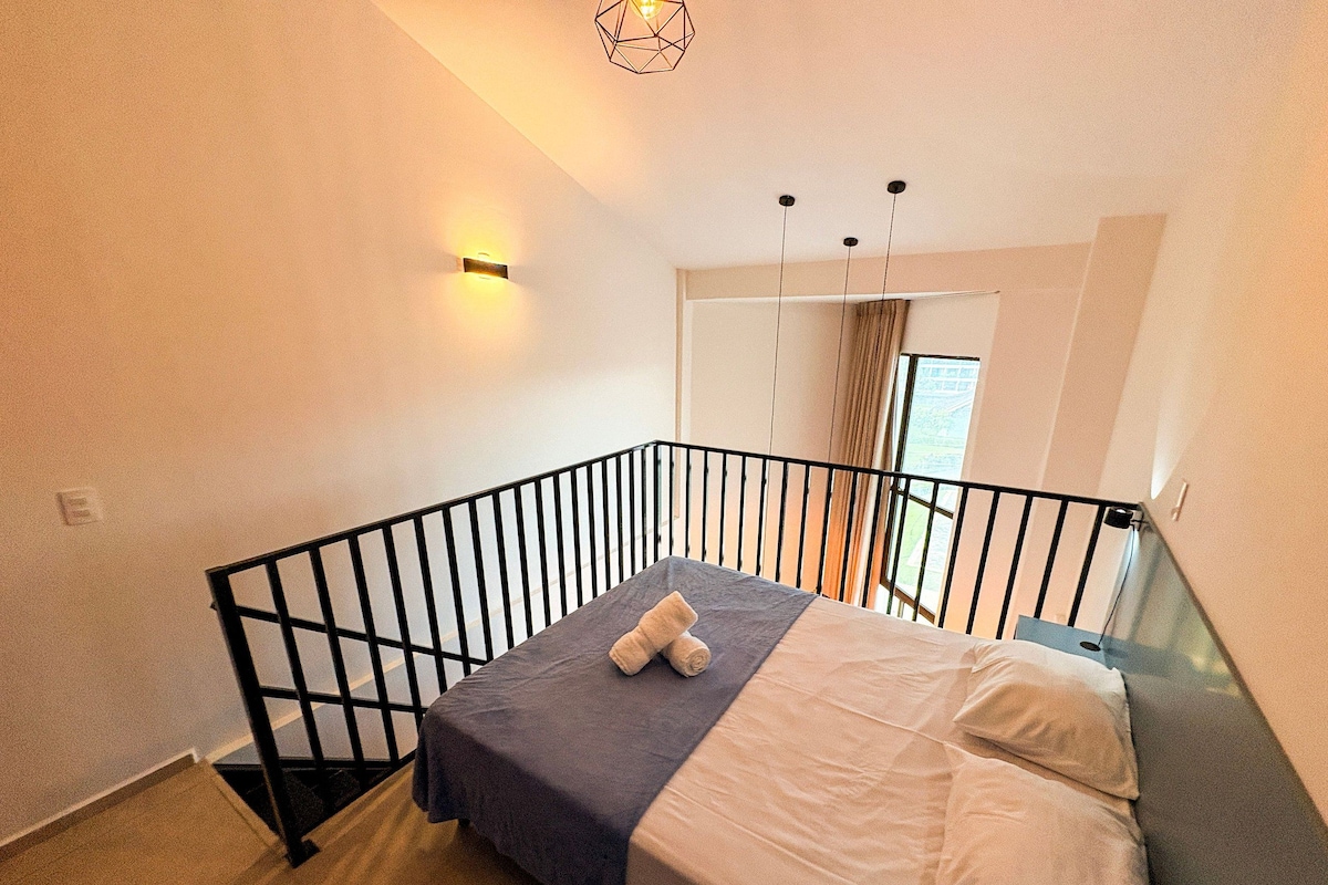 A bedroom with a bed, a window, and a balcony railing.