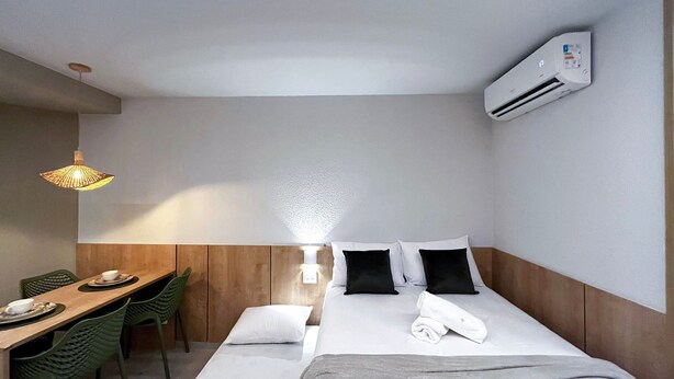 A hotel room with a bed, bedside table, chair, lamp, and an air conditioning unit. - Max Carneiros Suites - Praia dos Carneiros by CTA (Tamandaré)