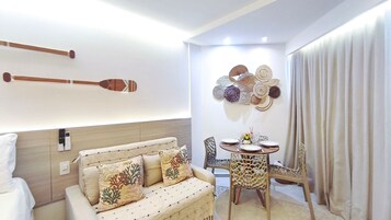 Habitación de hotel con sofá, una mesa de comedor con sillas, un adorno en la pared y una cortina.