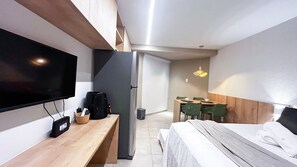 A compact hotel room with a bed, a desk, a television, a coffee maker, and a dining area with chairs. - Max Carneiros Suites - Praia dos Carneiros by CTA (Tamandaré)